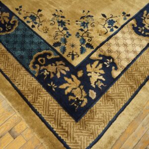 Gold rug with detailed navy and teal borders and floral accents rests on distressed wooden floorboards.