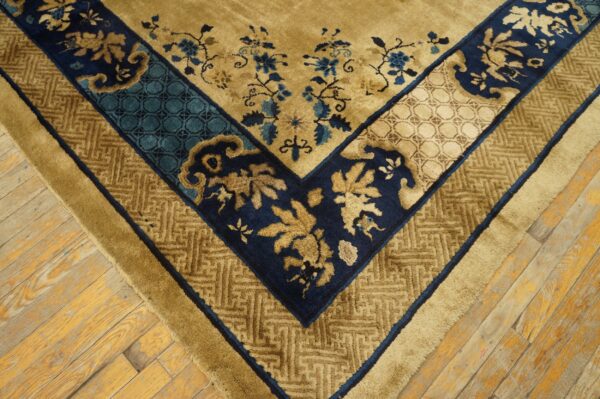 Gold rug with detailed navy and teal borders and floral accents rests on distressed wooden floorboards.