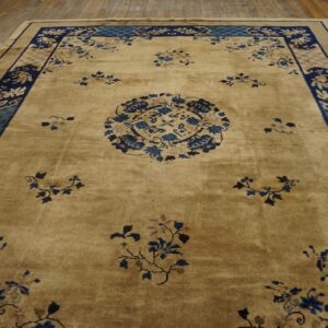 Tan rug with navy and teal borders and scattered blue floral patterns lying on rustic wooden planks.