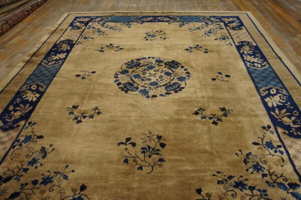 Tan rug with navy and teal borders and scattered blue floral patterns lying on rustic wooden planks.
