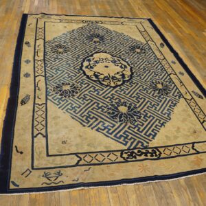 Beige rug featuring a large blue diagonal key pattern and floral medallions rests on distressed wood flooring.
