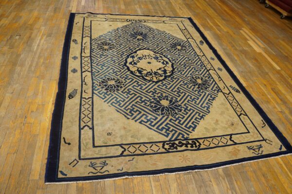 Beige rug featuring a large blue diagonal key pattern and floral medallions rests on distressed wood flooring.