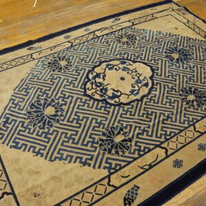 Beige and blue rug with geometric meander pattern and floral medallions on hardwood floor.
