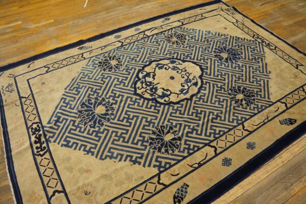 Beige and blue rug with geometric meander pattern and floral medallions on hardwood floor.
