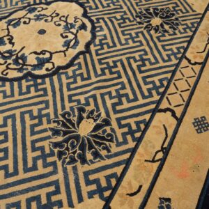 Tan rug with a blue Greek key geometric field pattern, floral medallions, and striped decorative borders.