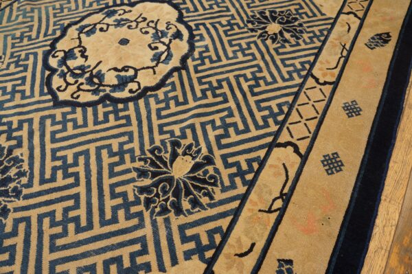 Tan rug with a blue greek key geometric field pattern, floral medallions, and striped decorative borders.