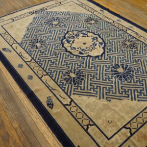 Beige rug with deep blue maze and floral patterns, framed by wide borders on wooden planks.
