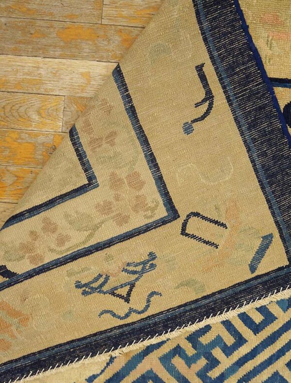Beige rug with navy borders and stylized motifs is folded back on weathered yellow plank flooring.