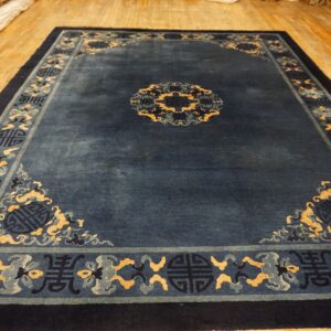 A lustrous indigo rug patterned with pale yellow and slate blue motifs sits on a wooden floor.