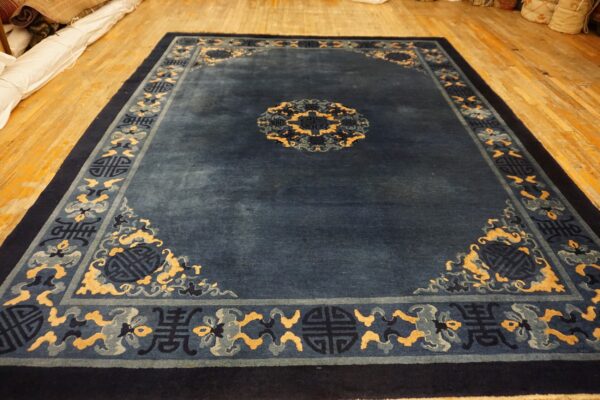 A lustrous indigo rug patterned with pale yellow and slate blue motifs sits on a wooden floor.