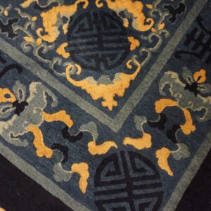 A deep blue rug featuring traditional gold and gray scrolling motifs and symbols rests on hardwood.