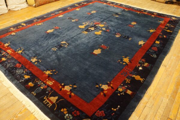 Large blue rug with scattered vase and floral patterns, featuring red and navy borders, on wood flooring.