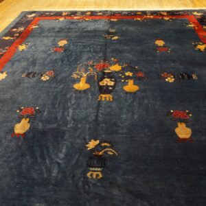 Dark blue rug featuring yellow and red floral vase motifs, bordered in red and navy, displayed on wood flooring.