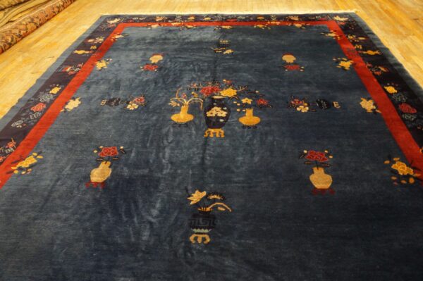 Dark blue rug featuring yellow and red floral vase motifs, bordered in red and navy, displayed on wood flooring.