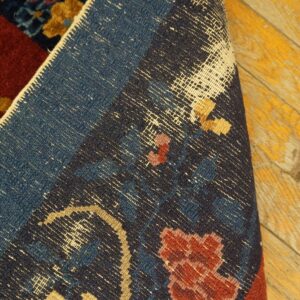 Detail of a dark blue and red floral patterned rug folded back, showing the woven structure on distressed yellow wood.