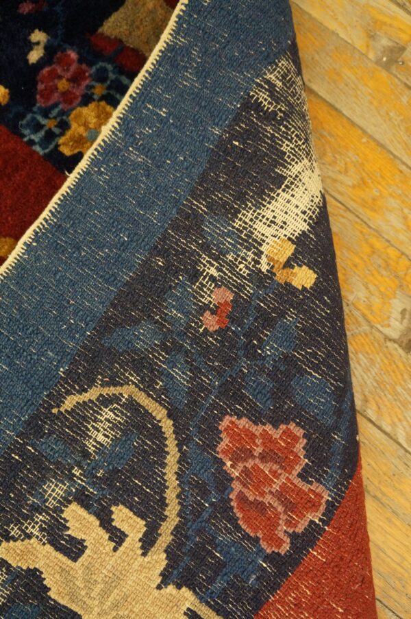 Detail of a dark blue and red floral patterned rug folded back, showing the woven structure on distressed yellow wood.