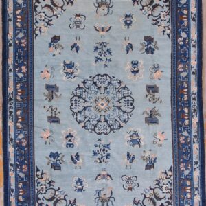 Light blue rug with a dark blue multi-layered border and scattered floral and emblematic motifs.