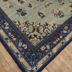 Blue and indigo rug corner with intricate floral and geometric patterns resting on worn light hardwood flooring.