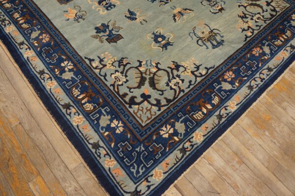 Blue and indigo rug corner with intricate floral and geometric patterns resting on worn light hardwood flooring.