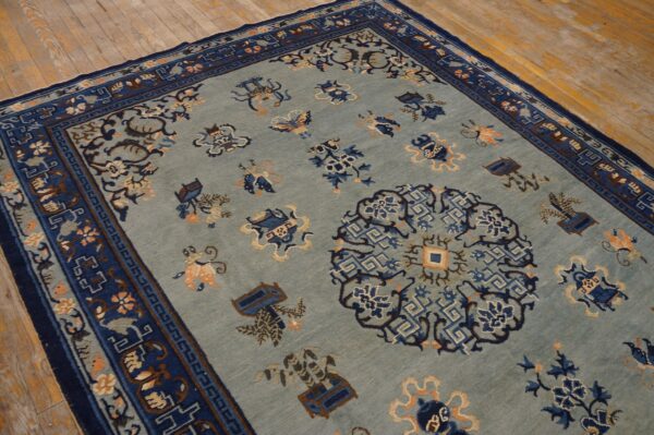 Light blue rug featuring scattered stylized motifs and a multi-layered navy border on worn wood flooring.