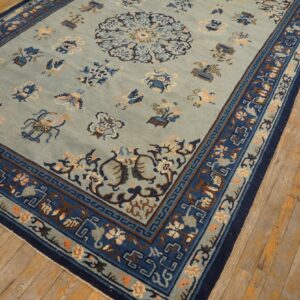 Slate blue rug featuring an ornate central pattern and layered dark blue borders on worn plank flooring.