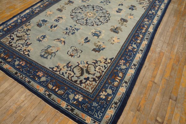 Slate blue rug featuring an ornate central pattern and layered dark blue borders on worn plank flooring.