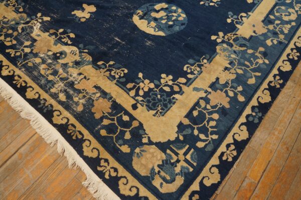 A worn navy blue rug with beige floral and vine patterns rests on rustic light brown plank flooring.