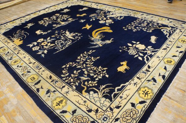 Detailed navy blue rug with gold and cream scenic motifs of birds, foliage, and animals on wood flooring.