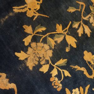 Deep blue rug texture showing gold, green, and orange floral and vine motifs in close detail.