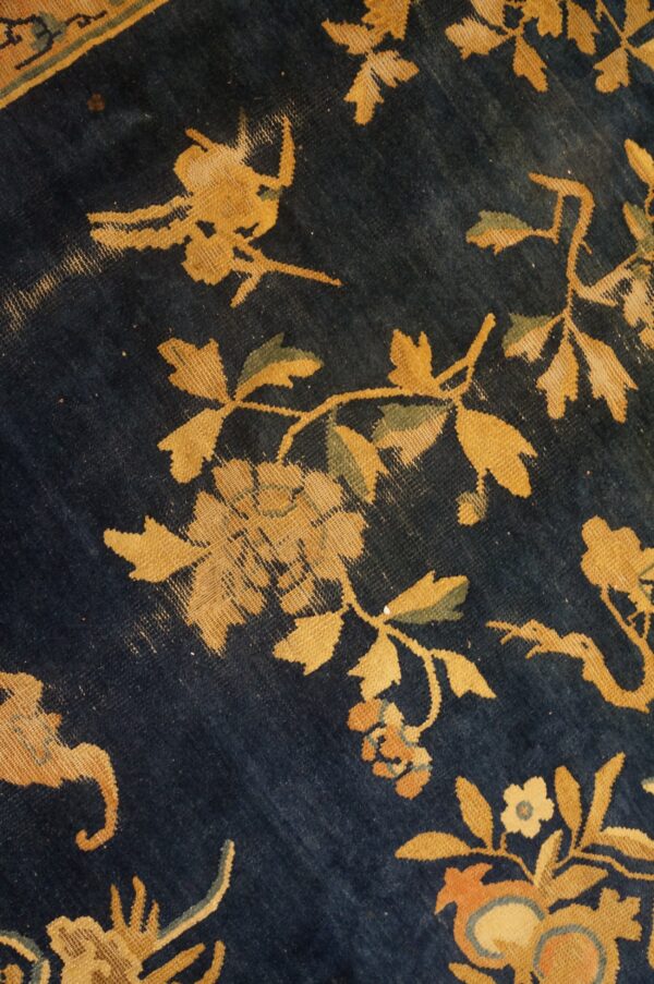 Deep blue rug texture showing gold, green, and orange floral and vine motifs in close detail.