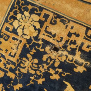 Navy blue and golden tan geometric patterns on a very worn rug with visible backing fibers.