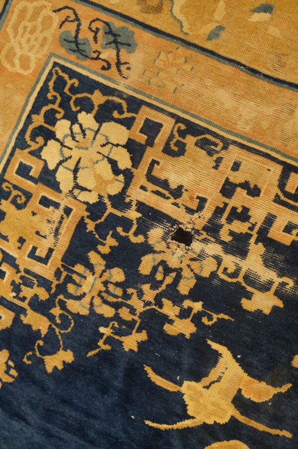 Navy blue and golden tan geometric patterns on a very worn rug with visible backing fibers.