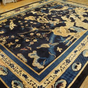 Ornate dark blue rug with tan bird and blossom motifs, shown on a rustic light wood floor.