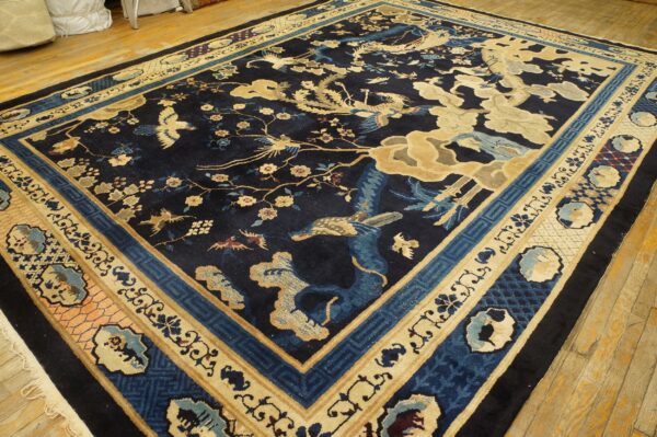 Ornate dark blue rug with tan bird and blossom motifs, shown on a rustic light wood floor.