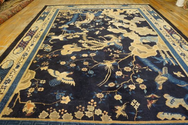 Dark blue rug featuring tan, blue, and gold scenic bird and floral motifs on wood flooring.