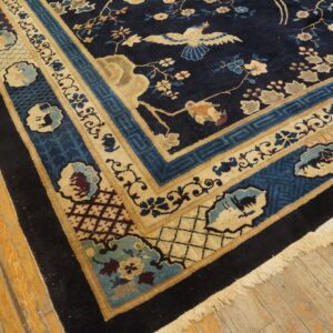 Navy blue rug with beige borders and colorful floral and bird motifs rests on worn yellow wood flooring.