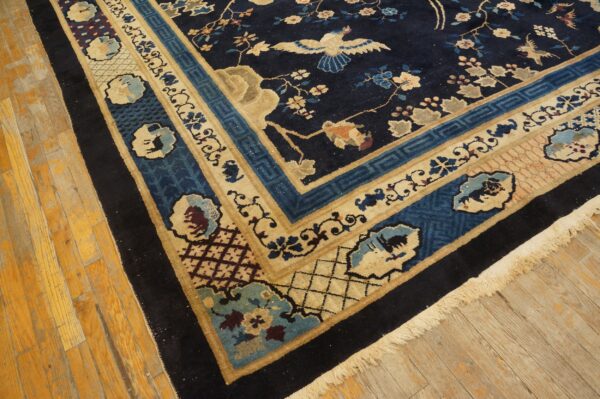 Navy blue rug with beige borders and colorful floral and bird motifs rests on worn yellow wood flooring.