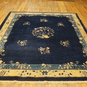 Rectangular, deep blue rug featuring a detailed gold and light blue floral medallion and thick borders on wood flooring.