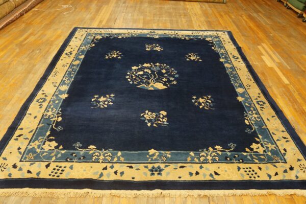 Rectangular, deep blue rug featuring a detailed gold and light blue floral medallion and thick borders on wood flooring.