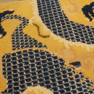 Low-pile rug close-up showing gold ground with navy blue scale-like patterning and cream details.