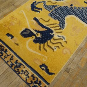 Golden yellow rug with a navy blue and tan stylized dragon pattern sits on distressed wooden flooring.