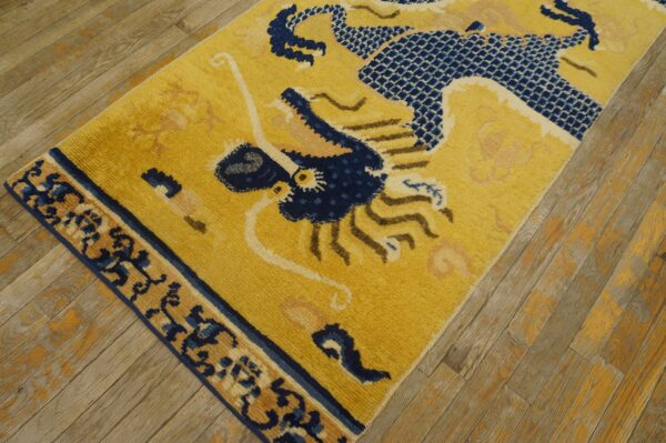 Golden yellow rug with a navy blue and tan stylized dragon pattern sits on distressed wooden flooring.