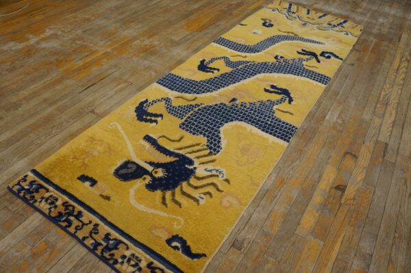 A yellow runner rug featuring a detailed navy blue dragon design rests on distressed wood flooring.