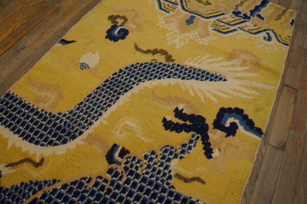 Medium-pile yellow rug features a dense navy blue dragon pattern laid over rustic wood flooring.