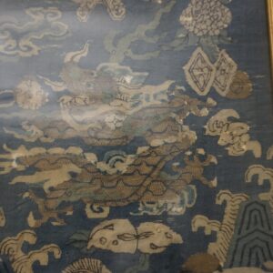 Framed textile featuring a low-pile blue ground with an elaborate tan dragon, cloud, and wave pattern.