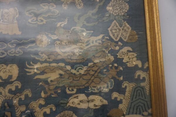 Framed textile featuring a low-pile blue ground with an elaborate tan dragon, cloud, and wave pattern.