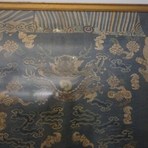 Dark blue textile in a gold frame features a stylized dragon and tan floral and cloud patterns.