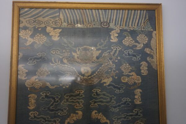 Dark blue textile in a gold frame features a stylized dragon and tan floral and cloud patterns.