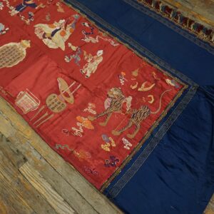 Red textile runner with detailed embroidered figures and a tiger, bordered by navy panels with gold trim, resting on wood floors.