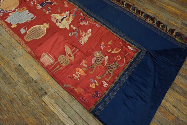 Red textile runner with detailed embroidered figures and a tiger, bordered by navy panels with gold trim, resting on wood floors.